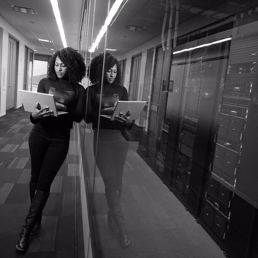 Woman standing with her laptop in front of a glassed server room